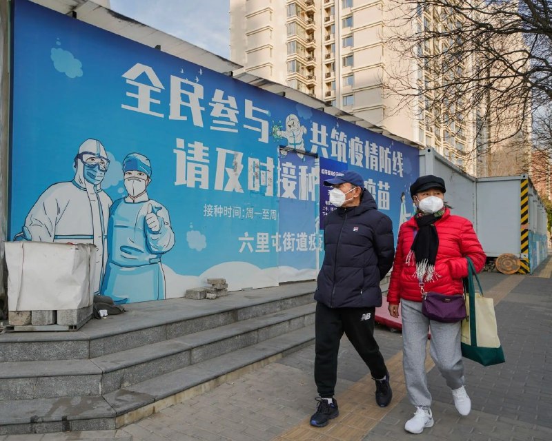 北京，一对夫妇走在防疫宣传墙前